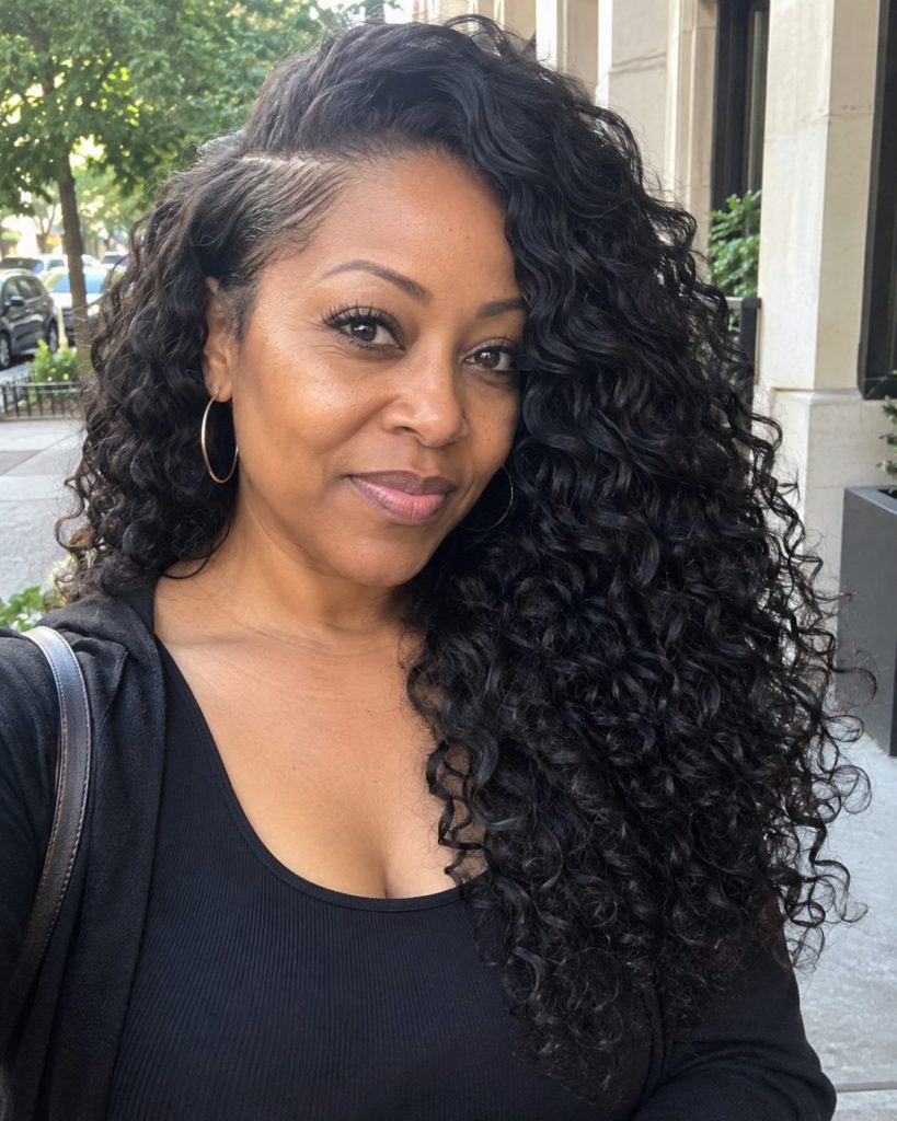 Long defined natural black curls styled with a deep side part in an outdoor street portrait