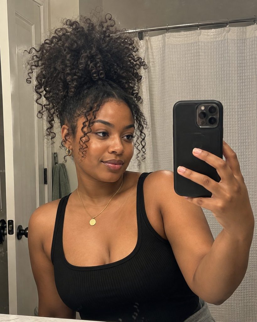 Long tight natural curls gathered into a high loose puff in a bathroom mirror selfie