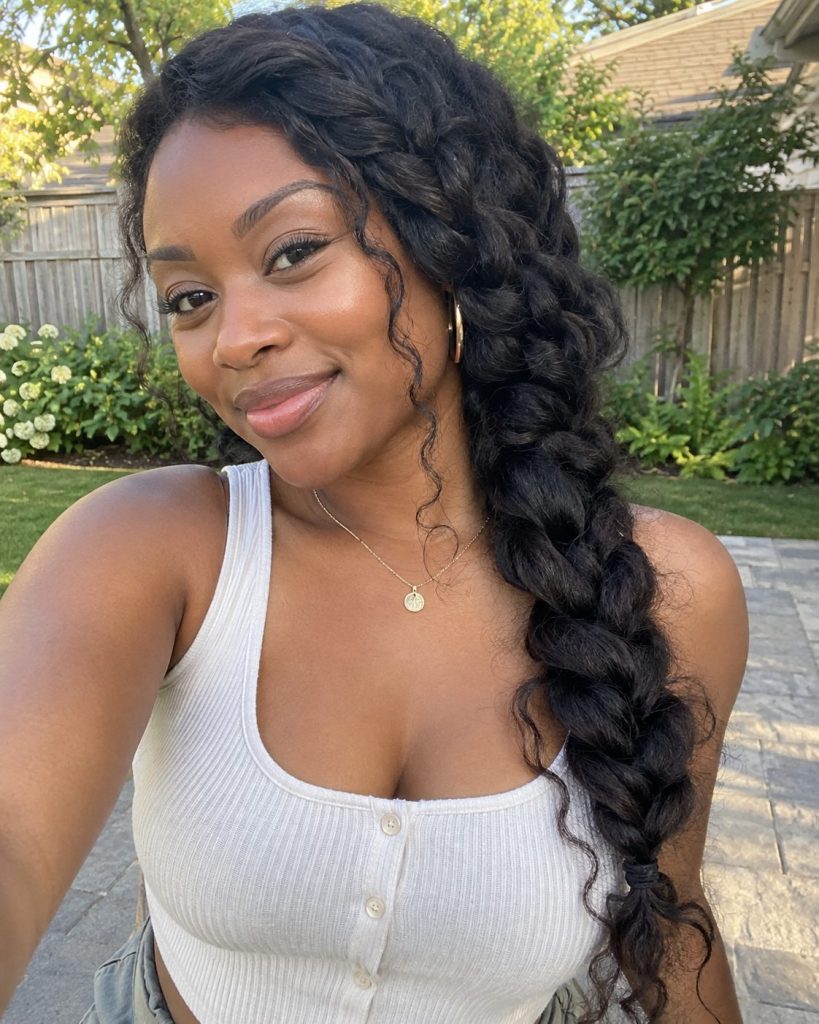A loose thick Dutch side braid on dark textured hair in a casual backyard portrait